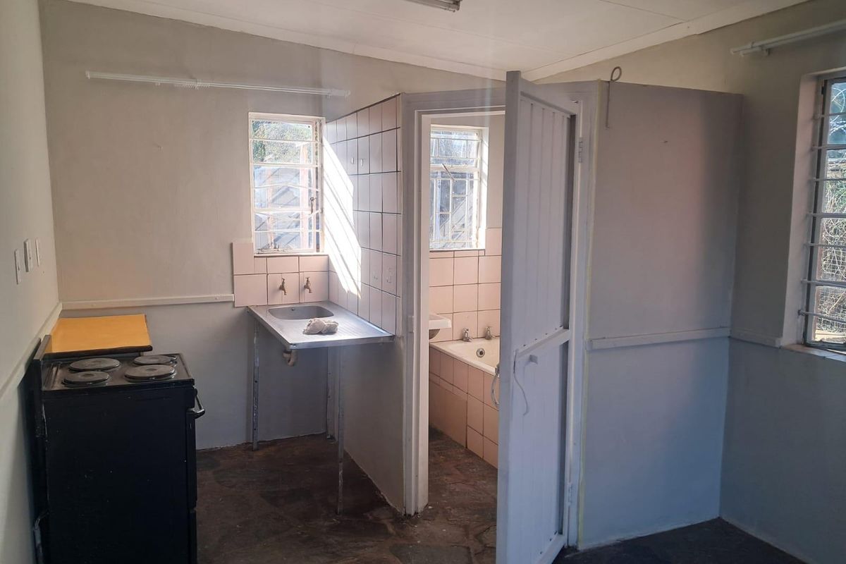 An open-plan area featuring a basic kitchenette with a stainless steel sink and an adjacent bathroom with a built-in bathtub.