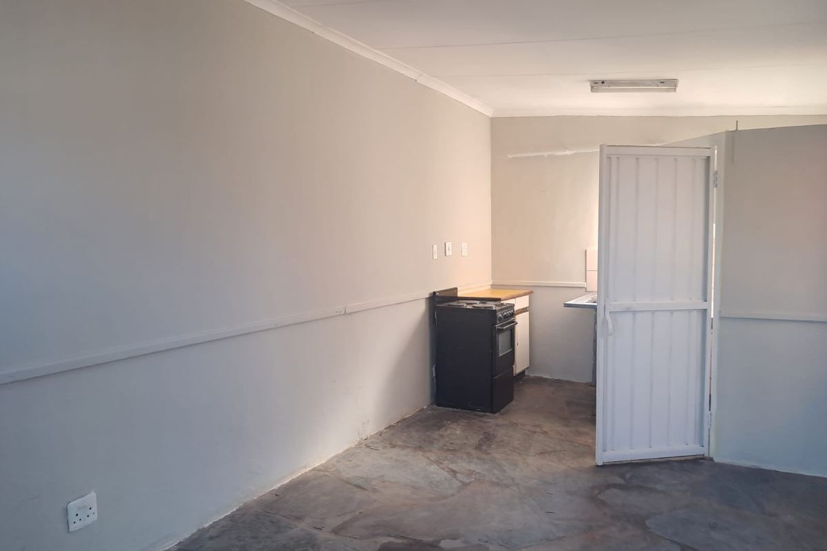 A basic, empty kitchen area featuring a freestanding stove, sink, and simple cabinetry, requiring cosmetic updates to improve its overall appeal.