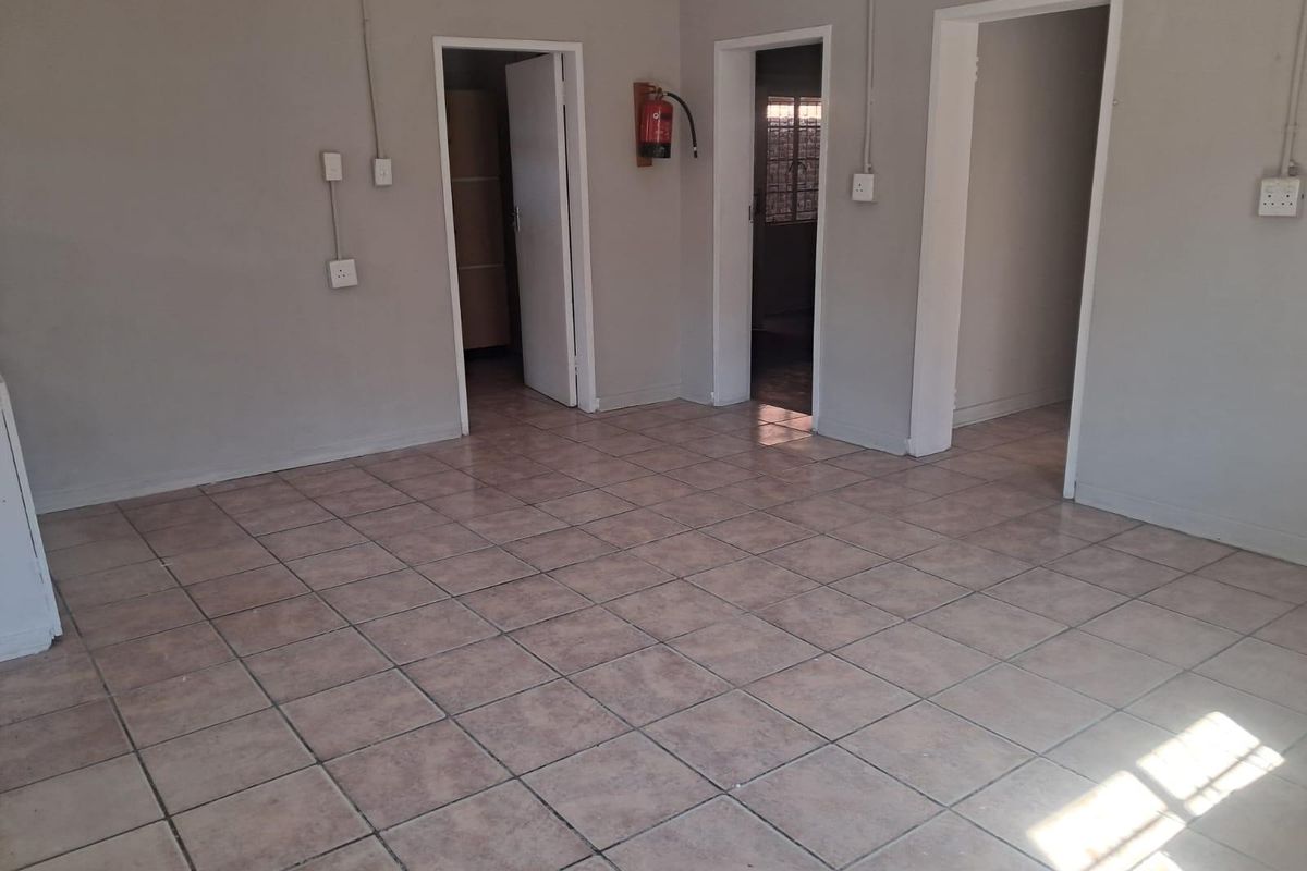 An empty, tiled living area featuring neutral walls, multiple internal doorways, and surface-mounted electrical conduits.