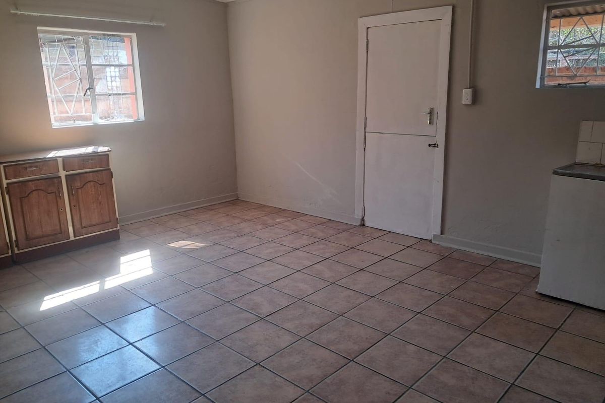 A vacant kitchen area featuring tiled flooring, built-in cabinetry, and security bars on the windows, offering a blank canvas for renovation.