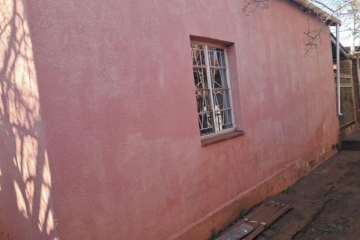 A side view of the property showing a textured pink exterior wall with security bars on the window and a drainage downpipe.