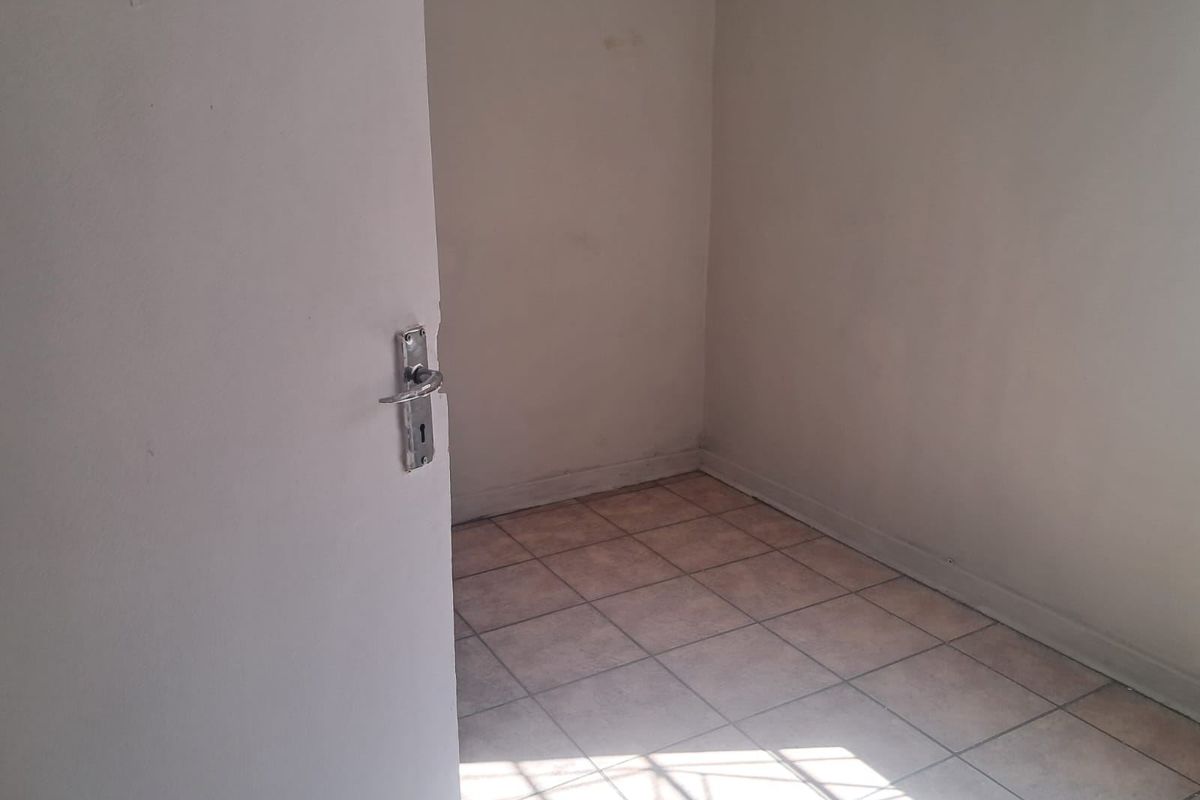 An empty, compact room featuring tiled flooring and plain walls, suitable for use as a bedroom or home office.