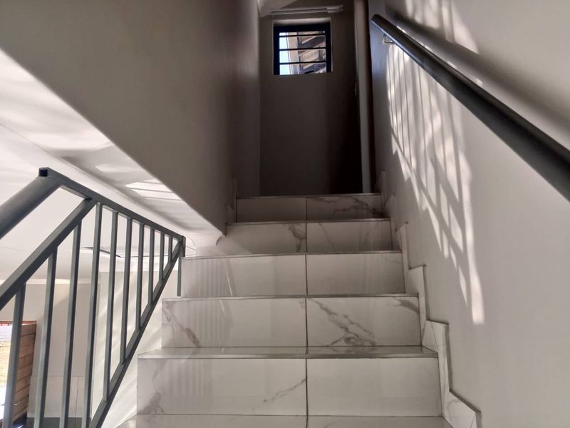 A bright staircase featuring modern white marble-look tiles and a sleek metal handrail leading to an upper level.