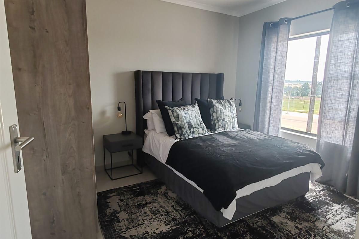 A modern bedroom featuring tiled flooring, a built-in wardrobe, and a large window providing natural light.