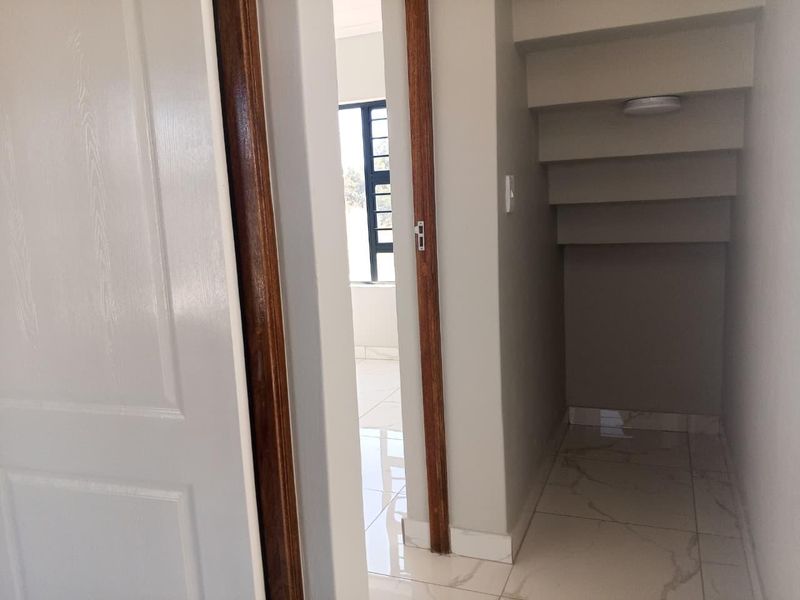 A clean, modern hallway featuring tiled flooring, wooden door frames, and a practical under-stair storage nook.