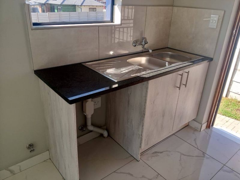 A functional scullery area featuring a stainless steel double sink, granite countertops, built-in cabinetry, and modern tiled flooring.