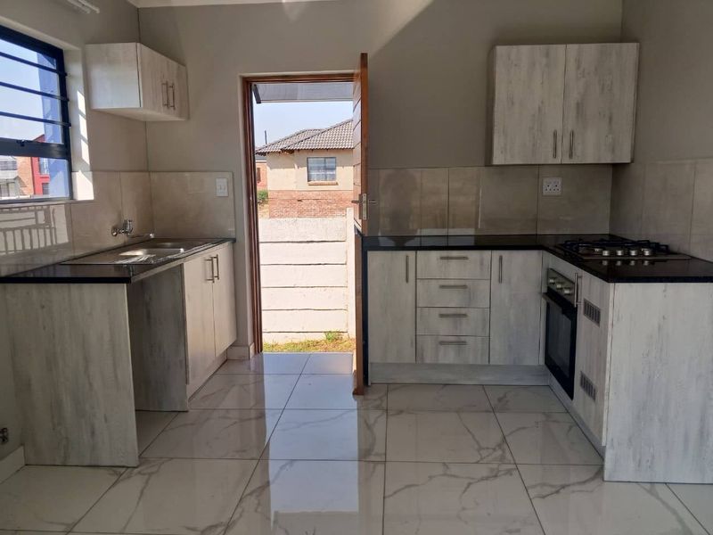 A modern, empty kitchen featuring light wood-grain cabinetry, dark granite countertops, a built-in oven, gas hob, and polished marble-look tiled flooring.