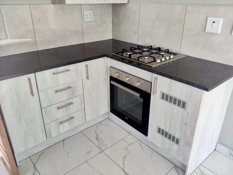 Modern kitchen corner featuring light wood-grain cabinetry, dark granite countertops, a built-in oven, gas hob, and elegant marble-look floor tiles.