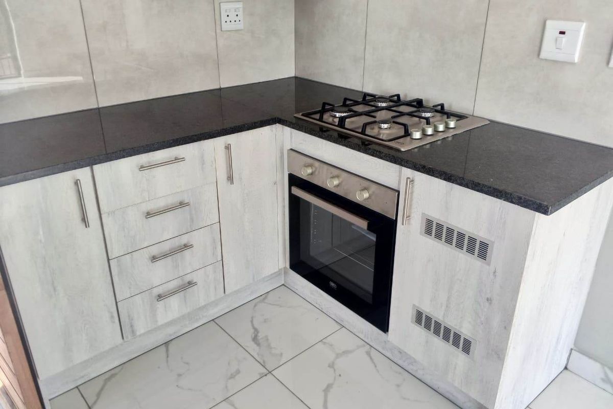 Modern kitchen corner featuring light wood-grain cabinetry, dark granite countertops, a built-in oven, gas hob, and elegant marble-look floor tiles.