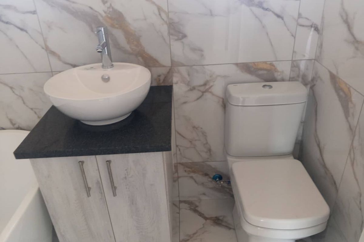 A modern bathroom featuring marble-look wall and floor tiles, a vessel sink on a granite-topped vanity cabinet, and a contemporary toilet.