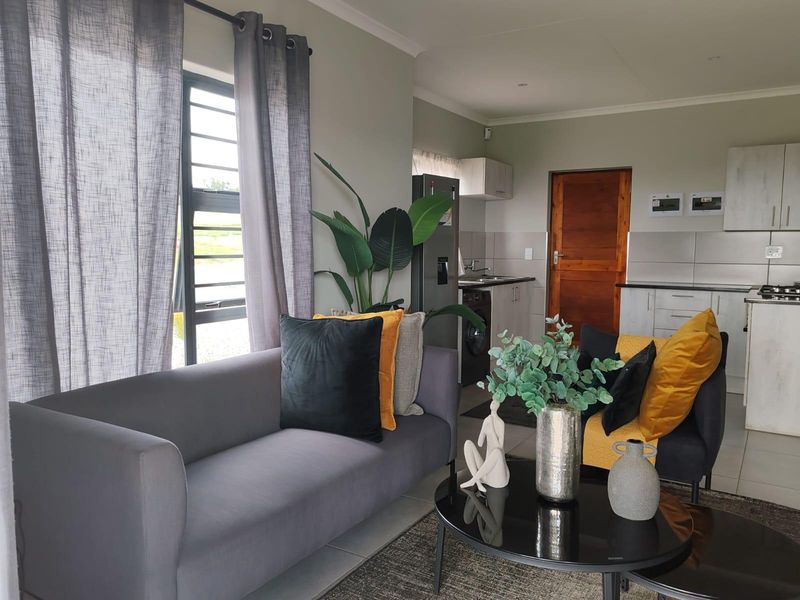Open-plan living area featuring tiled floors, modern kitchen cabinetry with integrated appliances, and large windows providing natural light.