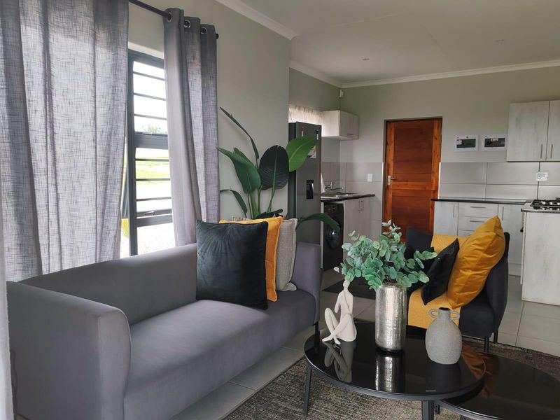 An open-plan living area featuring tiled floors, neutral walls, and an integrated kitchen with built-in cabinetry and modern finishes.