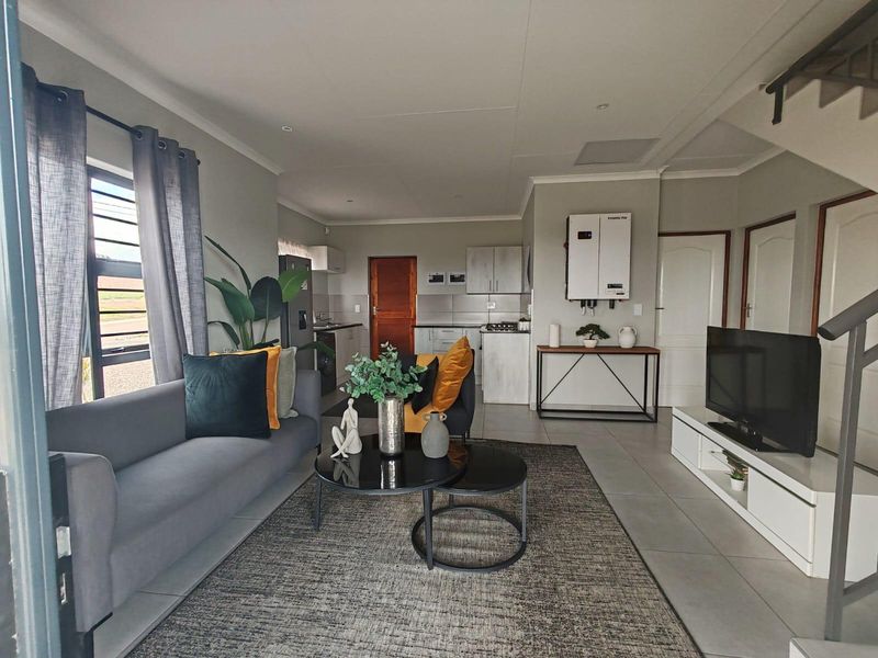 An open-plan living area featuring a modern kitchen, tiled floors, and a wall-mounted solar inverter system, creating a functional and contemporary living space.