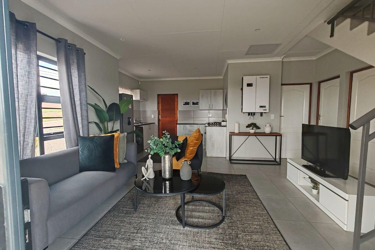 An open-plan living area featuring a modern kitchen, tiled floors, and a wall-mounted solar inverter system, creating a functional and contemporary living space.