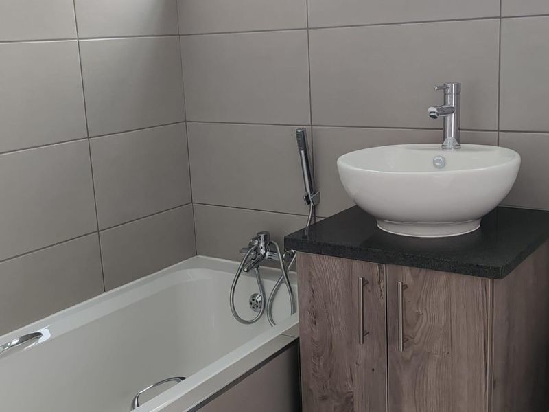 Modern bathroom featuring a floating wood-finish vanity with a vessel sink, a bathtub with chrome fixtures, and neutral wall tiling.