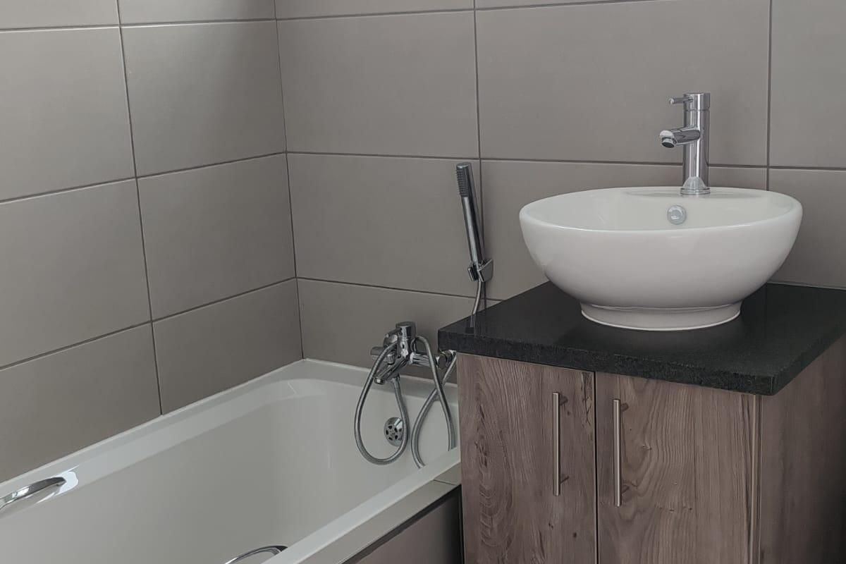 Modern bathroom featuring a floating wood-finish vanity with a vessel sink, a bathtub with chrome fixtures, and neutral wall tiling.