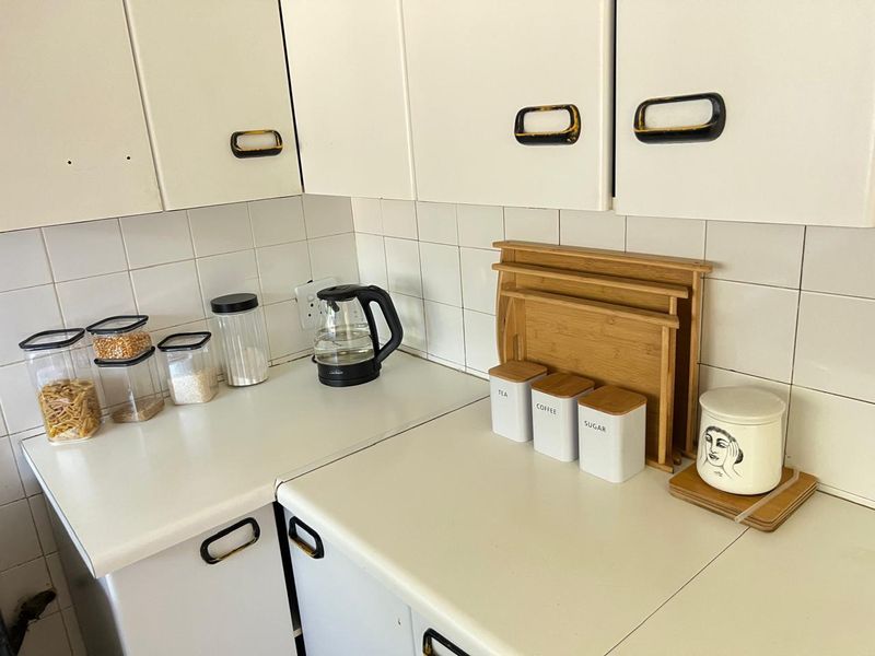 A compact kitchen area featuring white laminate cabinetry, tiled backsplash, and laminate countertops, showing signs of wear and dated finishes.