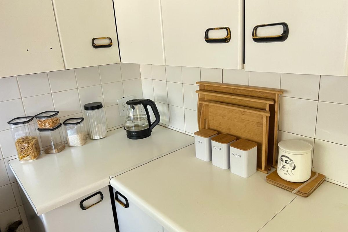 A compact kitchen area featuring white laminate cabinetry, tiled backsplash, and laminate countertops, showing signs of wear and dated finishes.