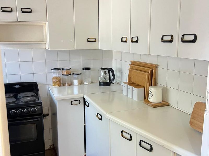 A compact kitchen featuring white cabinetry, tiled backsplash, and a freestanding electric stove, offering a functional layout with potential for modern updates.