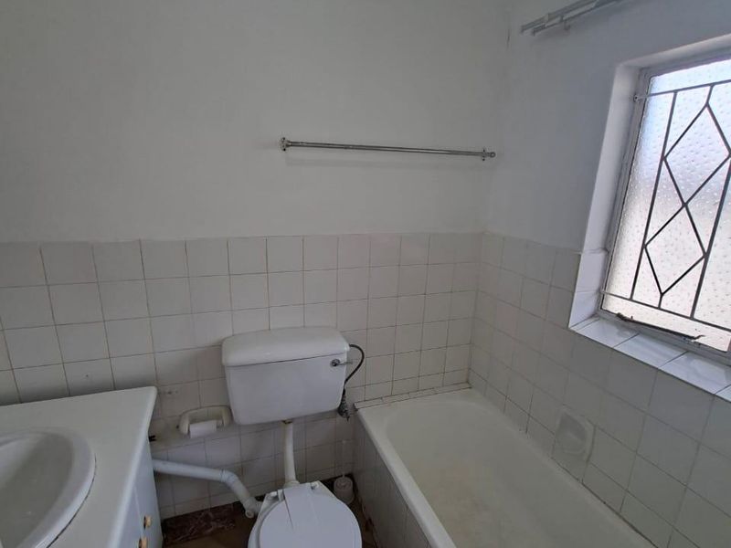 A dated bathroom featuring a built-in vanity, standard toilet, and bathtub with tiled splashbacks and flooring, requiring cosmetic updates.