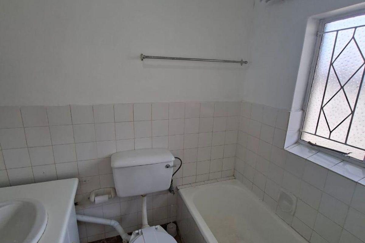 A dated bathroom featuring a built-in vanity, standard toilet, and bathtub with tiled splashbacks and flooring, requiring cosmetic updates.