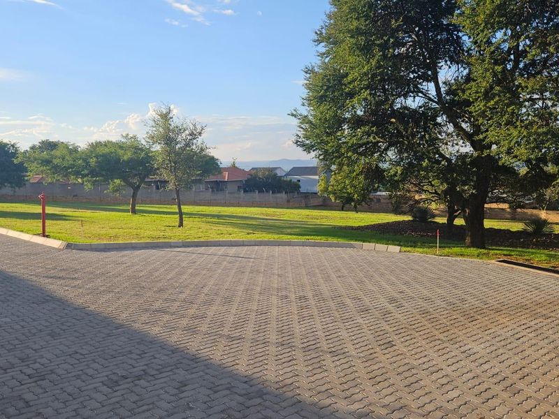 A view of a paved driveway leading to a well-maintained lawn and landscaped garden area with perimeter walling.