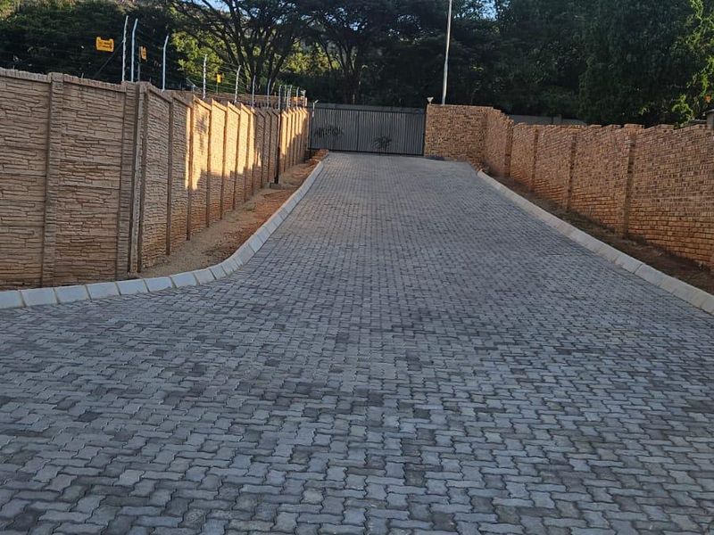 A paved driveway leading to a secure gated entrance, enclosed by high perimeter walls with electric fencing.