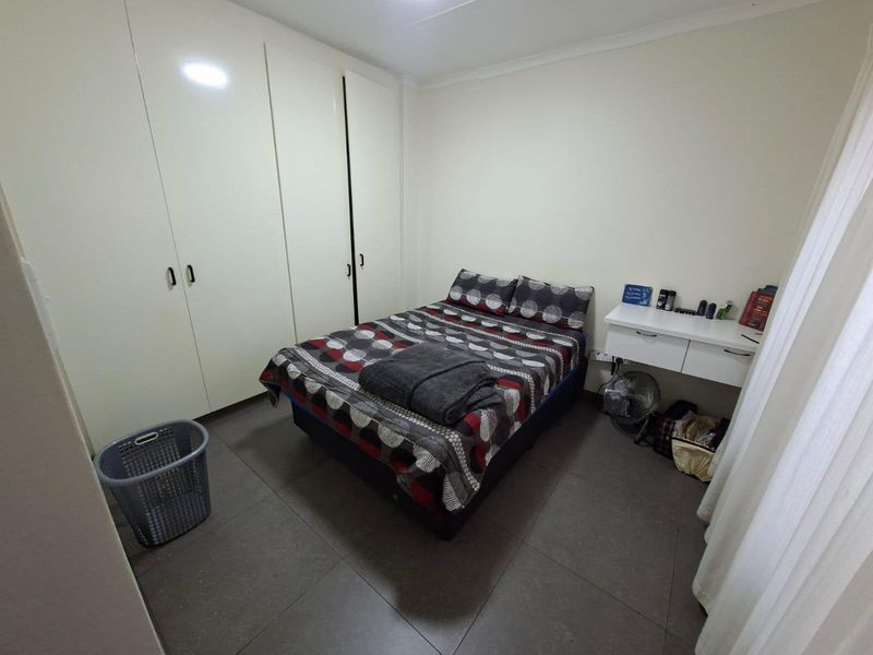 A functional bedroom featuring built-in cupboards, tiled flooring, and a wall-mounted floating desk, offering a practical and clean living space.