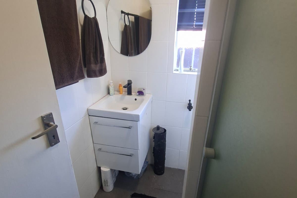 A compact, well-maintained bathroom featuring a modern wall-mounted vanity, basin with mixer tap, and neutral wall tiling.