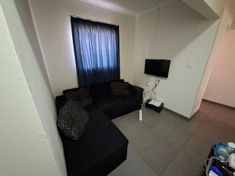 A compact living area featuring tiled flooring and coved ceilings, currently utilized as a casual lounge space.