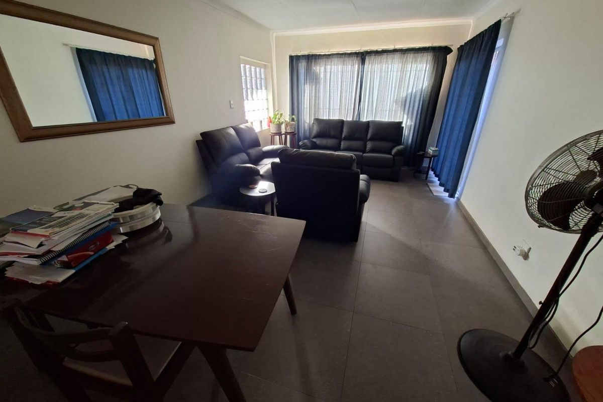 A living room featuring large format floor tiles and a unique glass block window, providing a functional and neutral space for relaxation.