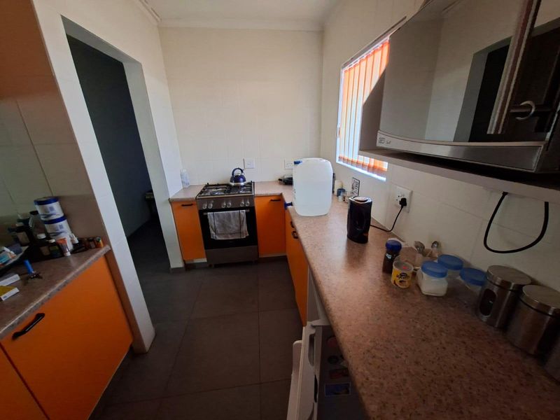 A functional kitchen featuring orange cabinetry, gas stove, and laminate countertops with tiled flooring and vertical window blinds.