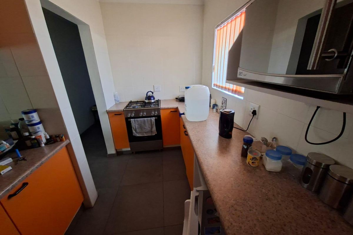 A functional kitchen featuring orange cabinetry, gas stove, and laminate countertops with tiled flooring and vertical window blinds.