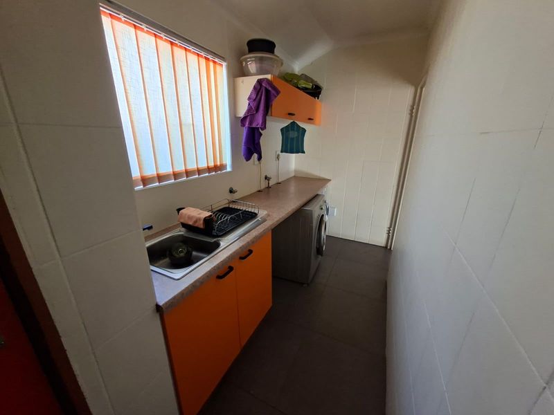 Functional laundry room featuring tiled walls and flooring, built-in cabinetry with laminate countertop, and a stainless steel sink.