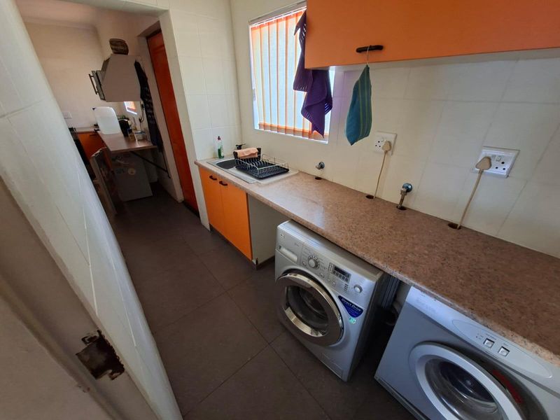Functional laundry area featuring built-in cabinetry, laminate countertops, a stainless steel sink, and dedicated plumbing connections for appliances.
