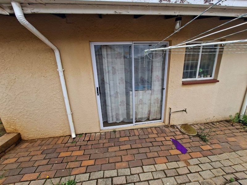 Rear exterior view featuring a paved patio area, sliding glass door access, and external water tap, showing signs of wear on the eaves and walls.