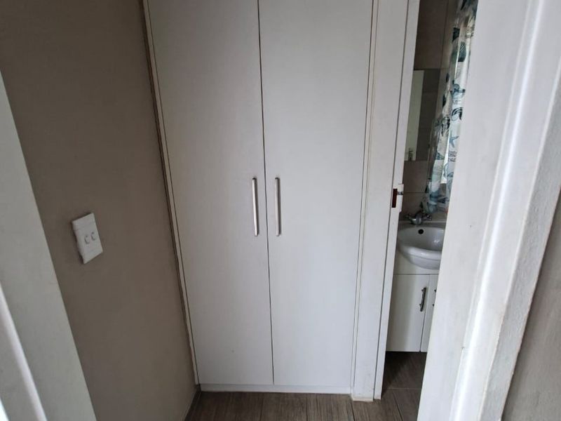 A clean hallway featuring neutral tiled flooring and a built-in storage cupboard, with a partial view into an adjacent bathroom.