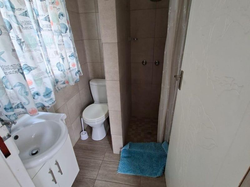 A functional bathroom featuring a vanity cabinet with basin, a toilet, and a tiled shower enclosure with a shower head.