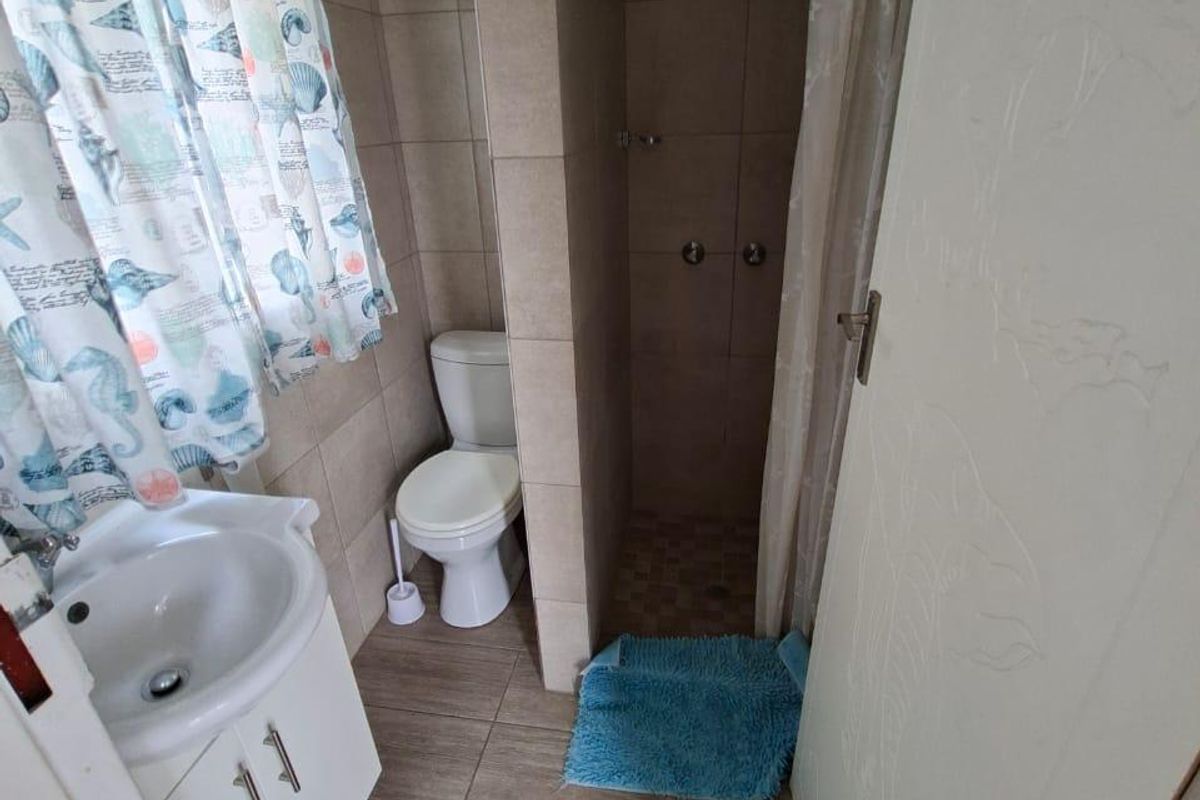A functional bathroom featuring a vanity cabinet with basin, a toilet, and a tiled shower enclosure with a shower head.