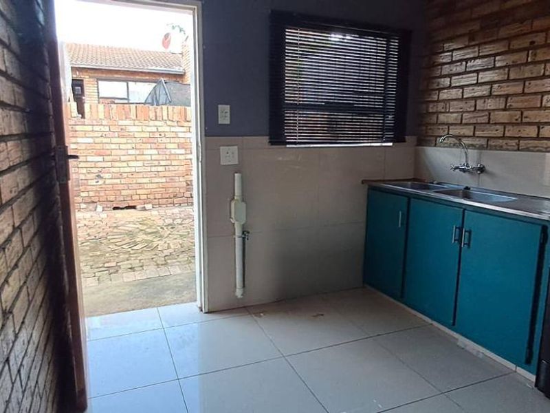 A functional kitchen featuring exposed brick walls, tiled flooring, built-in cabinetry, and direct access to an outdoor paved area.