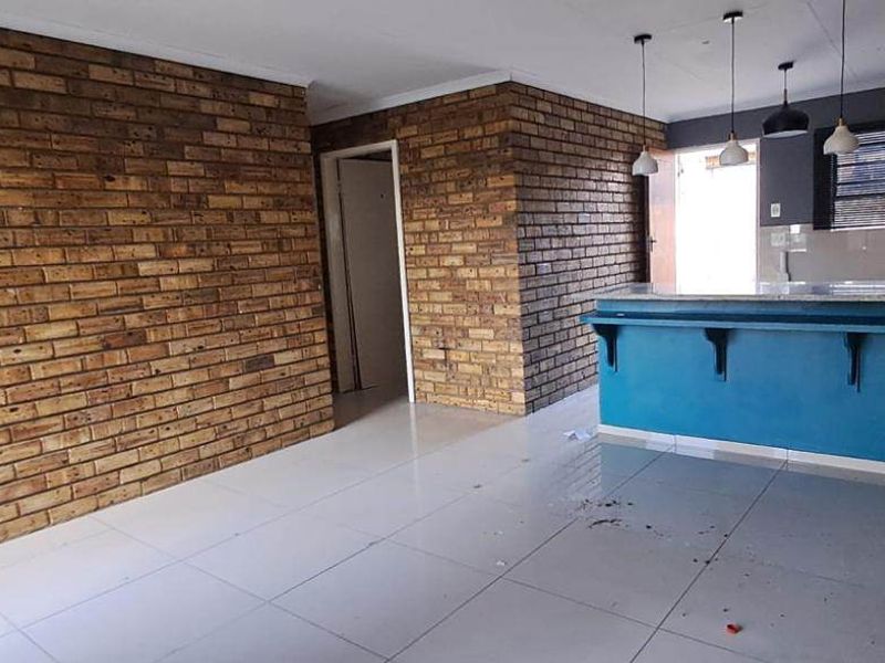 Open plan living and kitchen area featuring exposed brick walls, tiled flooring, and a breakfast bar with granite countertop.
