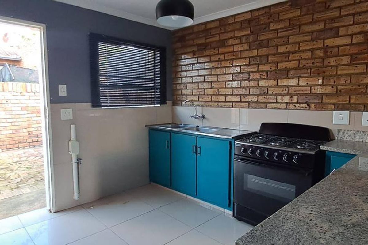 A functional kitchen featuring exposed brick walls, granite countertops, a stainless steel sink, and a freestanding gas stove with direct access to the rear exterior.