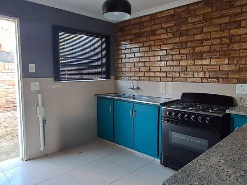 A functional kitchen featuring exposed brick walls, granite countertops, a stainless steel sink, and a freestanding gas stove with direct access to the rear exterior.
