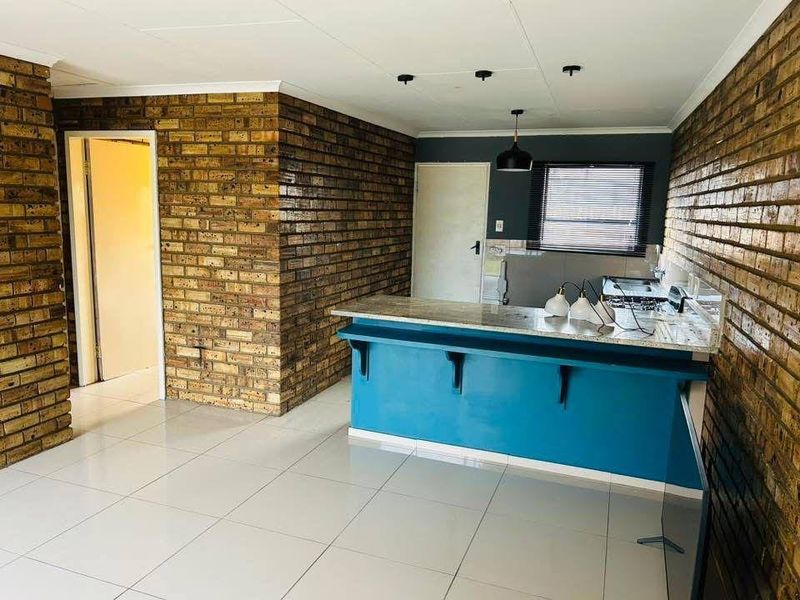 Open plan kitchen area featuring exposed brick walls, tiled flooring, and a breakfast bar with granite countertops.