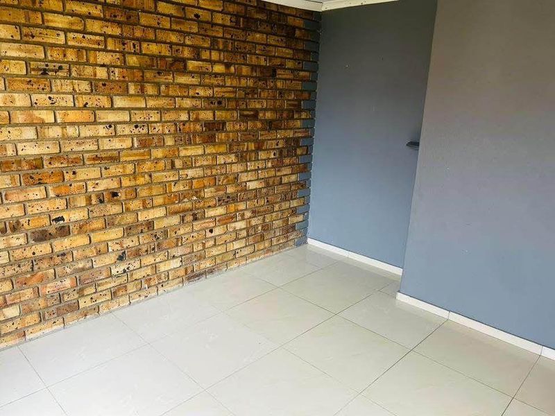 An empty living area featuring a rustic exposed brick feature wall and neutral tiled flooring, offering a blank canvas for interior design.