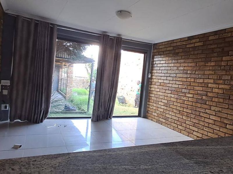 An empty living area featuring exposed brick walls, tiled flooring, and large sliding glass doors providing access to the outdoor space.