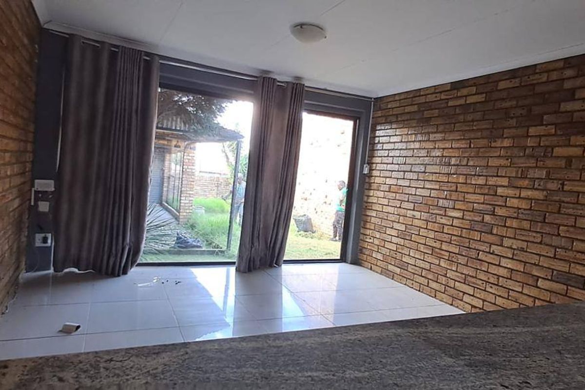 An empty living area featuring exposed brick walls, tiled flooring, and large sliding glass doors providing access to the outdoor space.