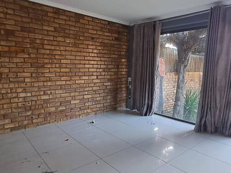 Empty living room featuring an exposed brick feature wall, large sliding glass doors providing natural light, and tiled flooring.