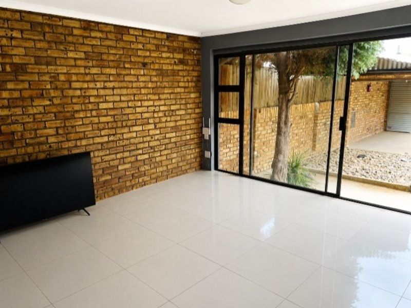 Bright living area featuring a rustic exposed brick wall, modern white tiled flooring, and large sliding doors providing seamless access to the outdoor space.