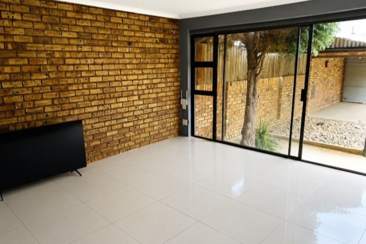 Bright living area featuring a rustic exposed brick wall, modern white tiled flooring, and large sliding doors providing seamless access to the outdoor space.